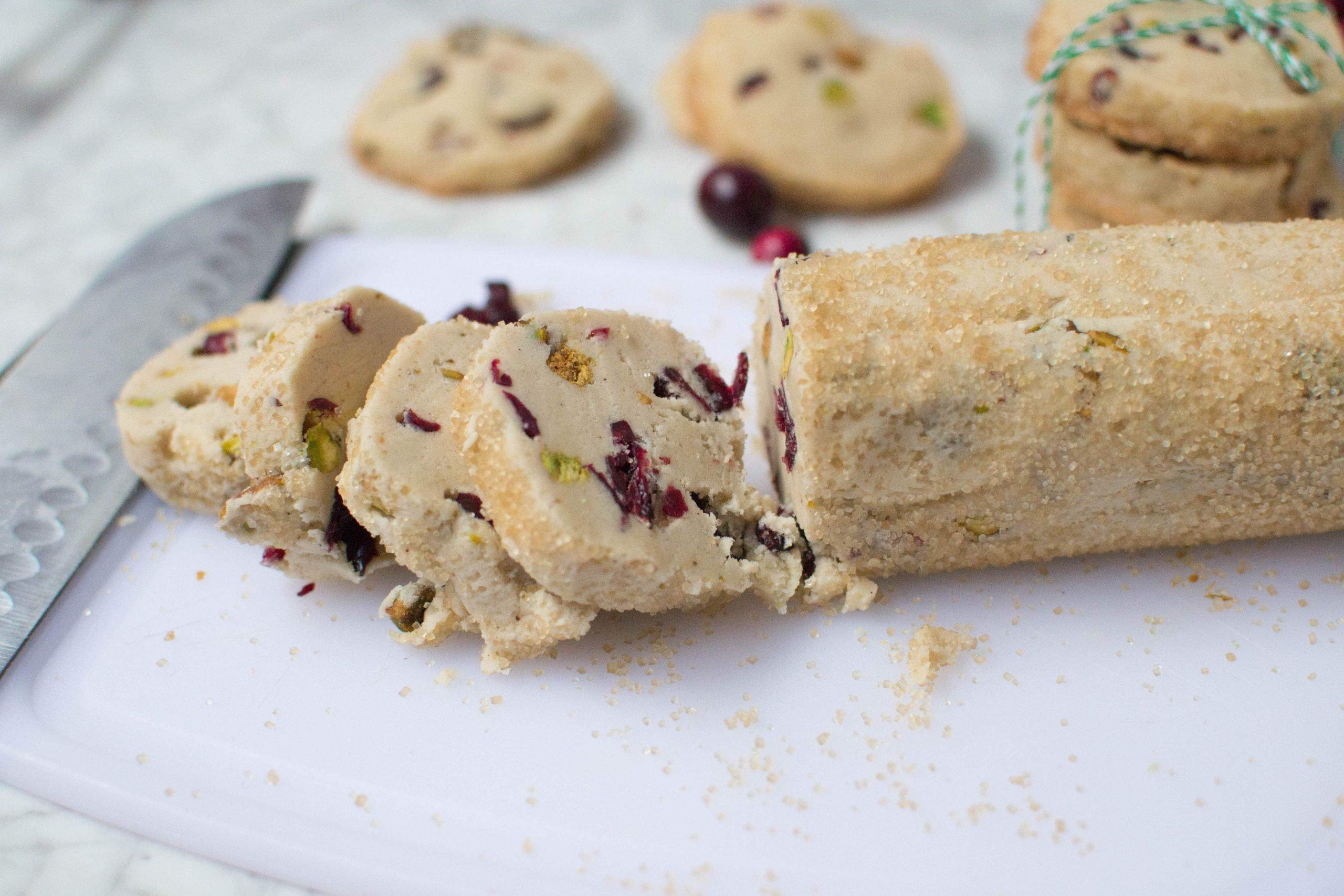 A log of raw cranberry pistachio cookie dough that has three slices cut off from it. 