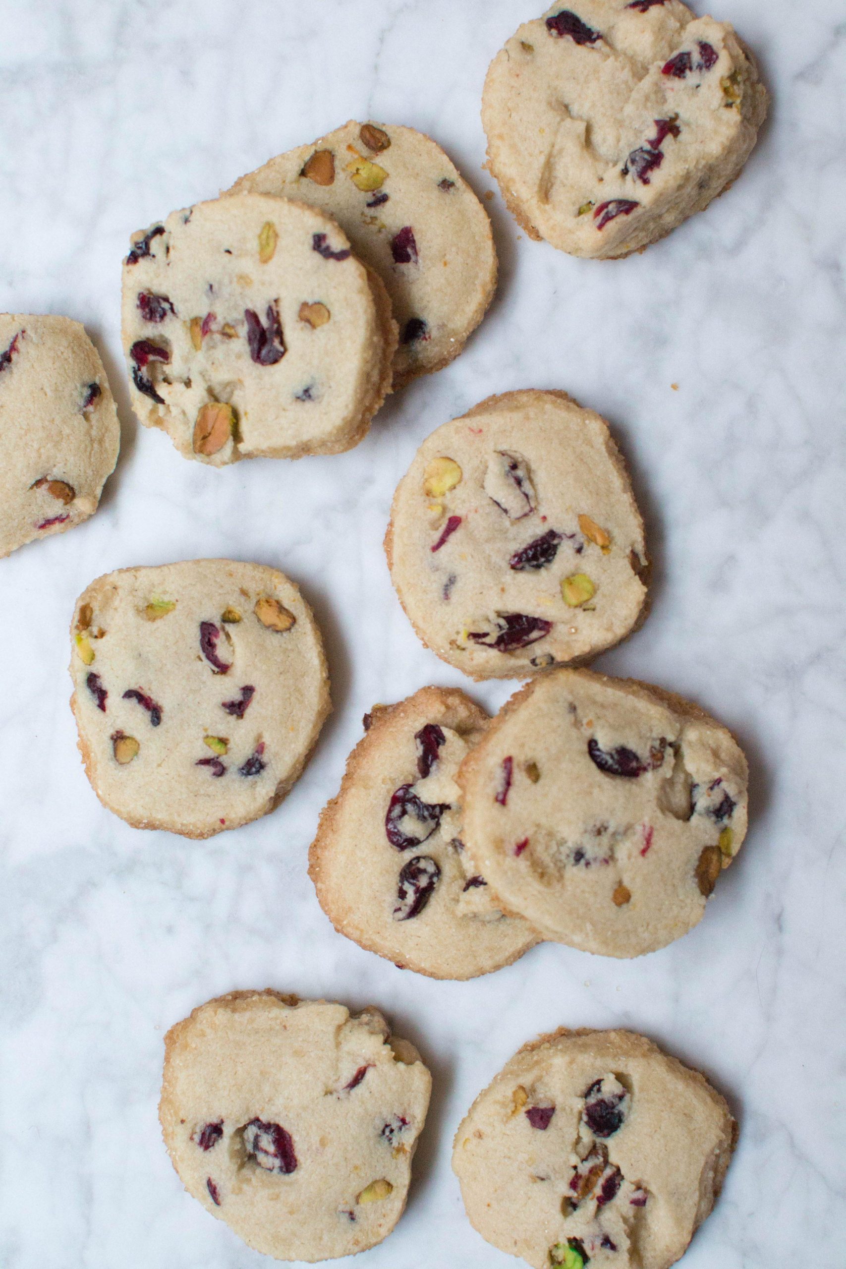 Cranberry pistachio shortbread cookies scattered on a marble surface. 