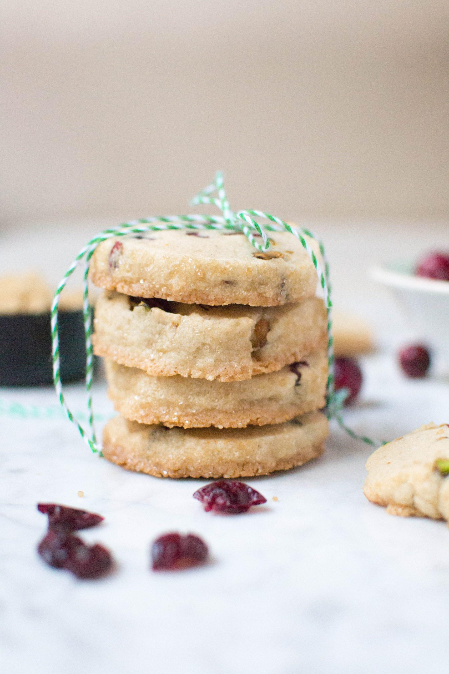 A stack of cranberry pistachio cookies tied with green and white twine. 