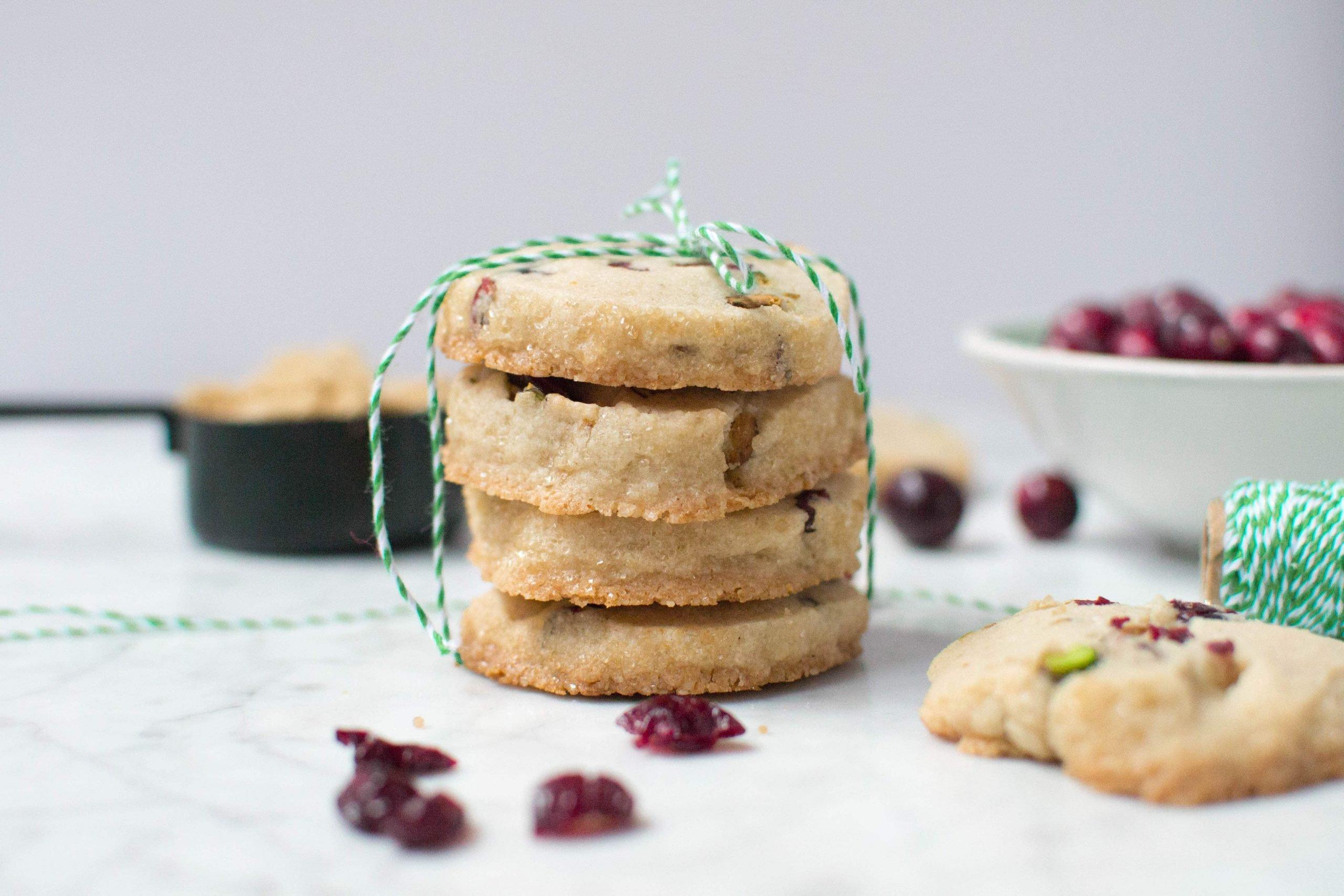 A stack of four pistachio cranberry shortbread cookies tied with green and white twine. 