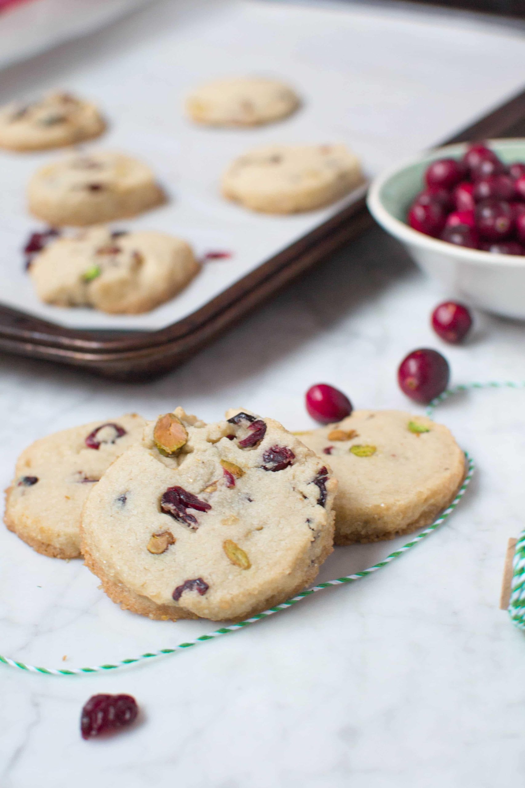 Three cranberry pistachio cookies layered on top of each other with a baking sheet in the background. 