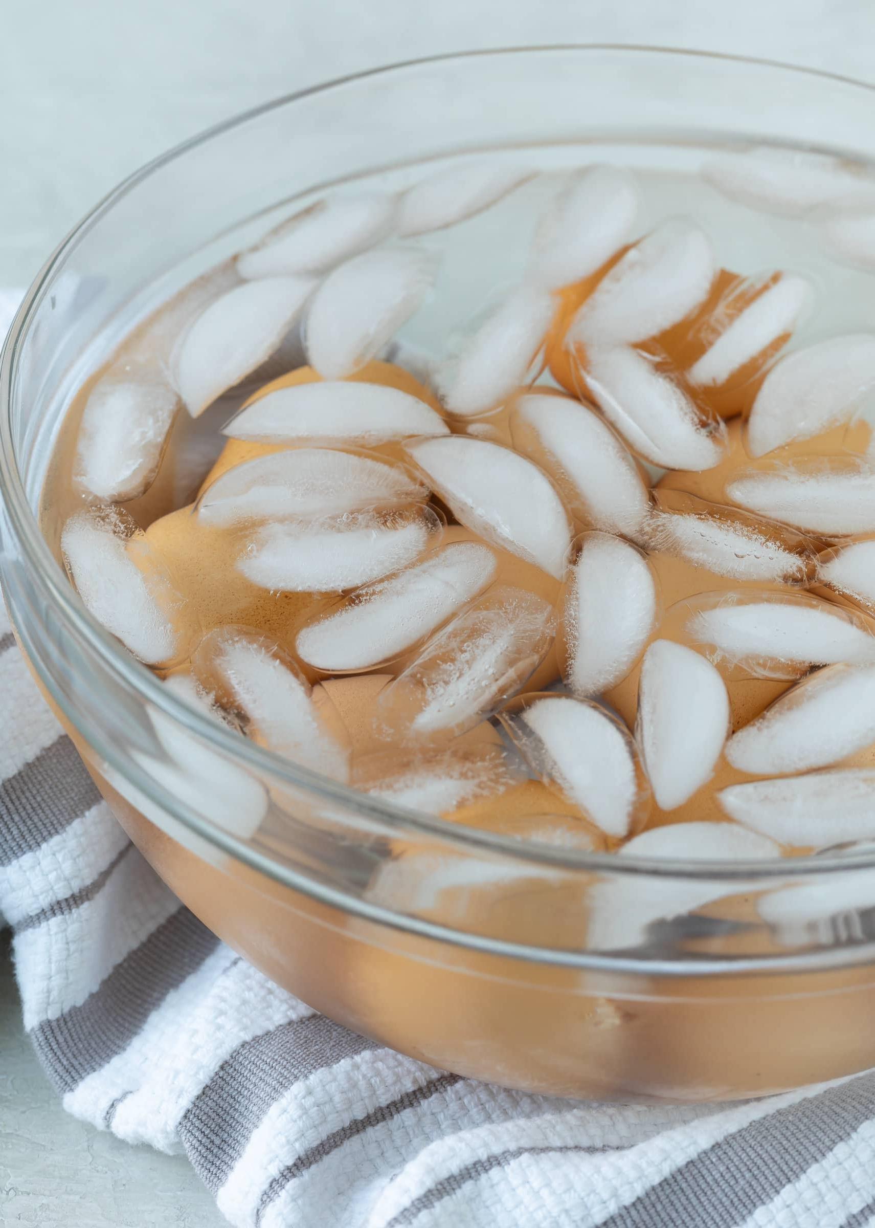 A glass bowl with ice cubes and water chilling down hard boiled eggs in an ice bath after boiling.