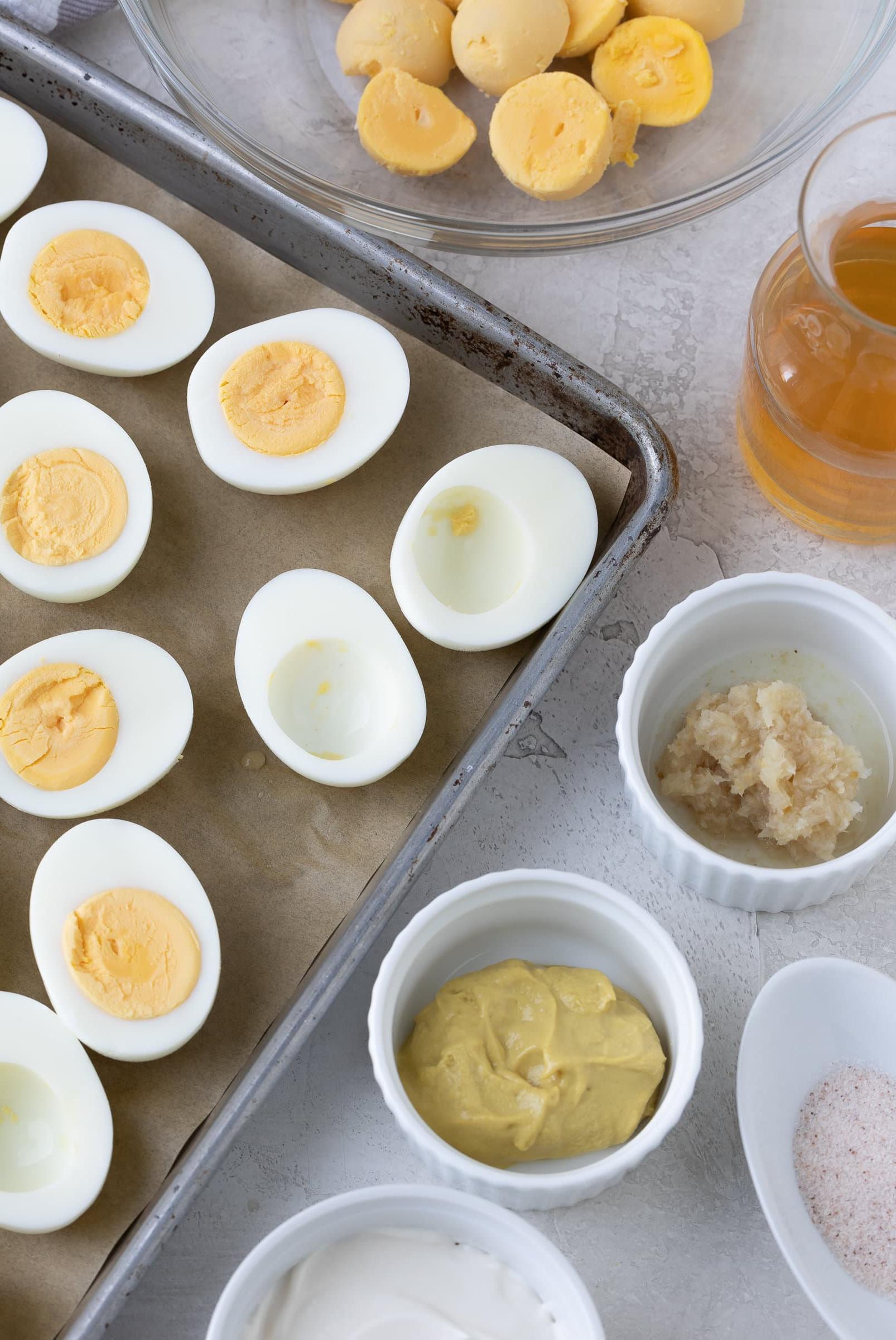 A baking sheet with hard boiled egg halves for making deviled eggs, with yolks, vinegar, mustard.