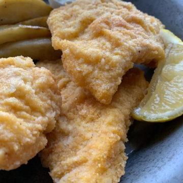 Three pieces of fried cod on a metal plate.