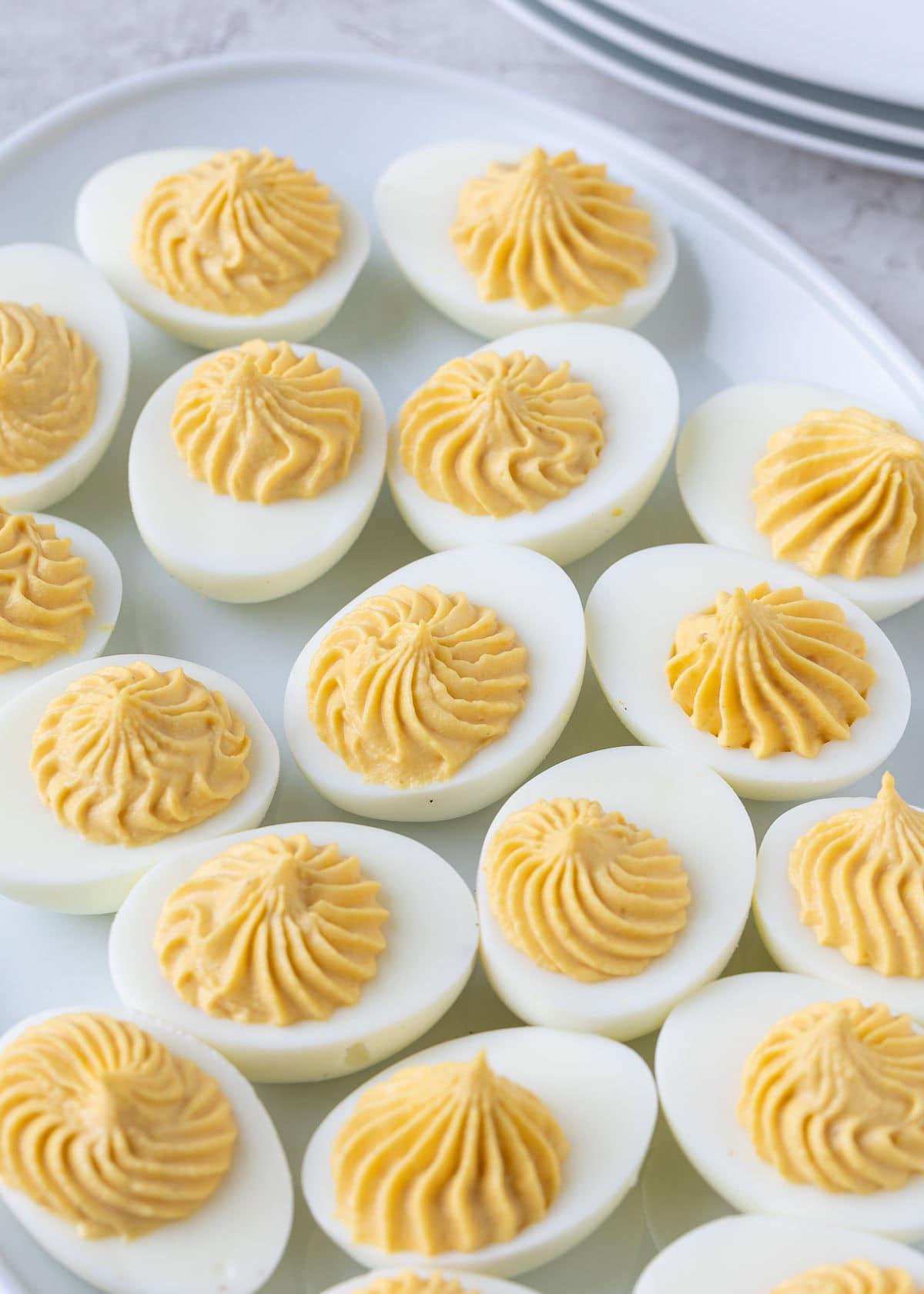 A plate of deviled egg halves after piping yellow filling in a decorative pattern.