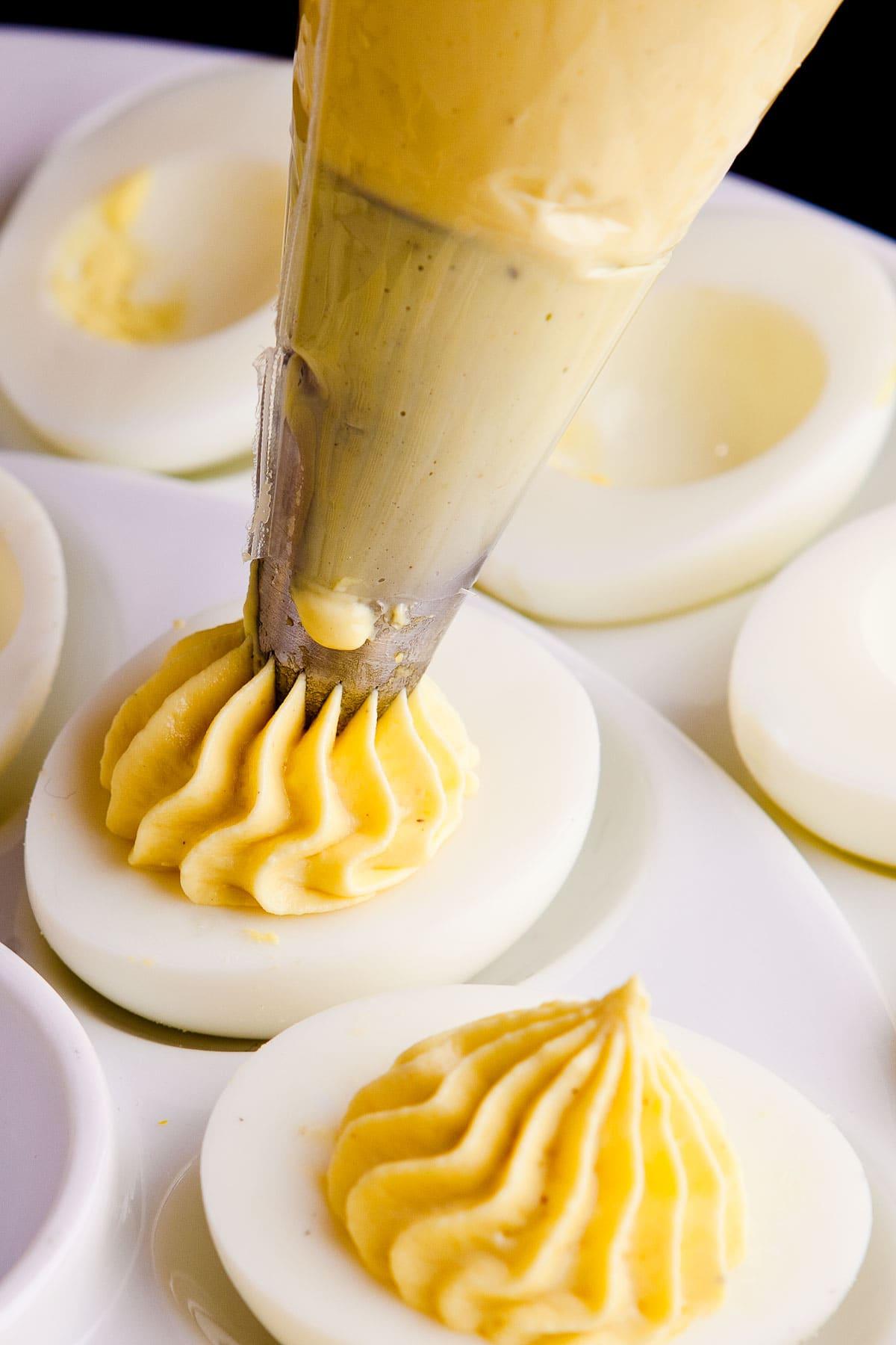 Deveiled Eggs-1761 Piping yellow egg filling into hard boiled egg halves for deviled eggs.