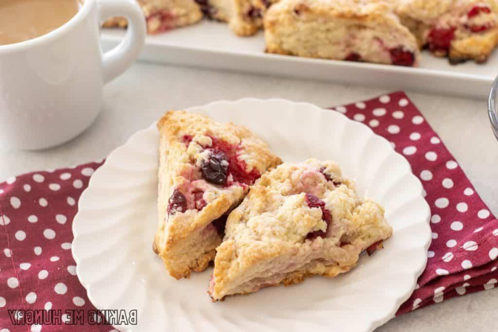 white chocolate cranberry scones with cut of coffee next to it and platter of scones behind